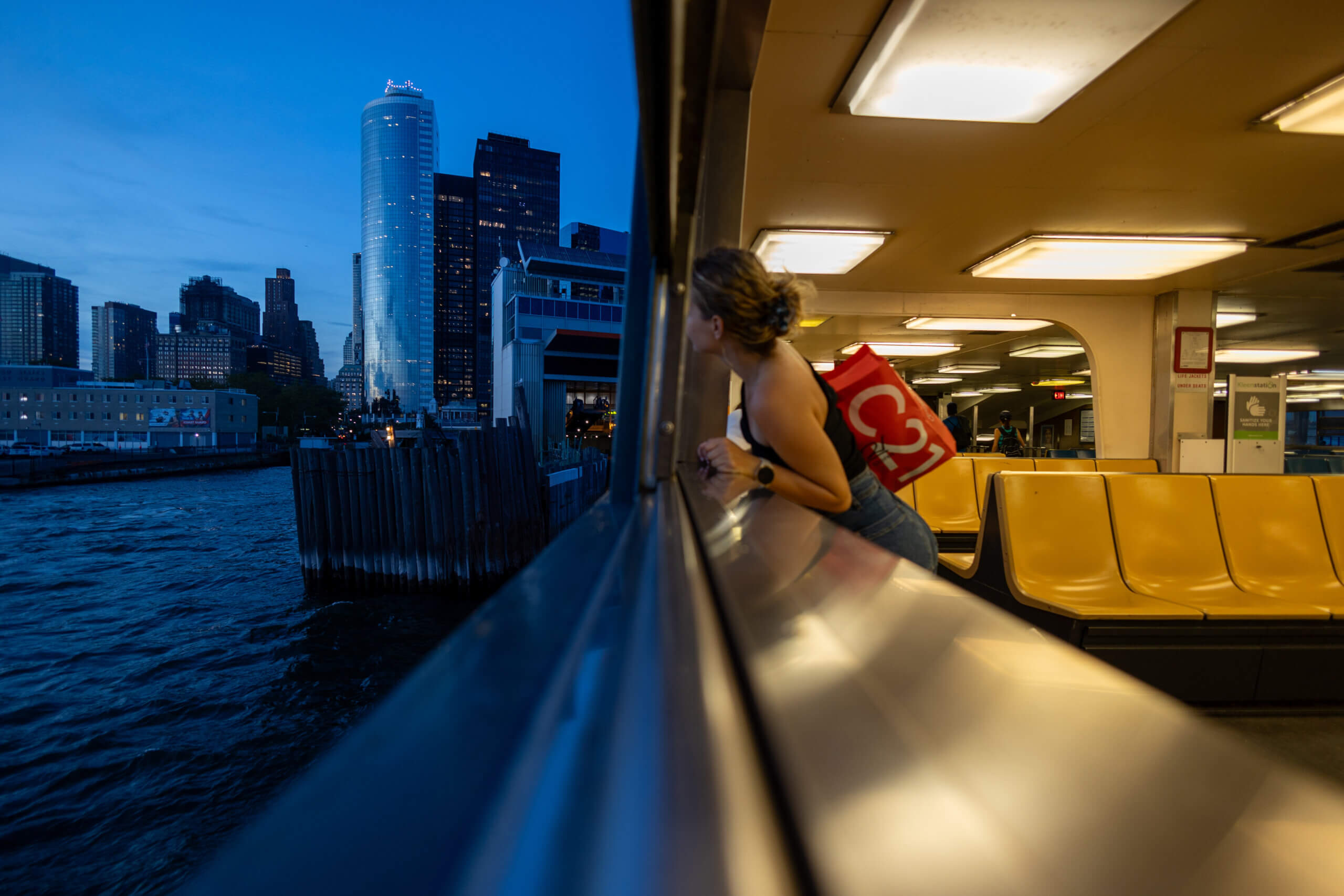 A photo taken from the boat returning from Staten Island at twilight, with warm interior tones and cool tones reflecting on the Manhattan skyscrapers in the distance