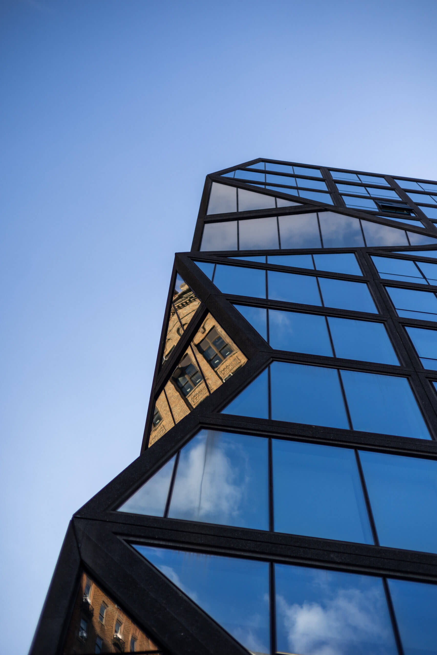 A photo of a New York building with reflective architecture, capturing the sky on one side and surrounding buildings on the other, showcasing urban design and reflections