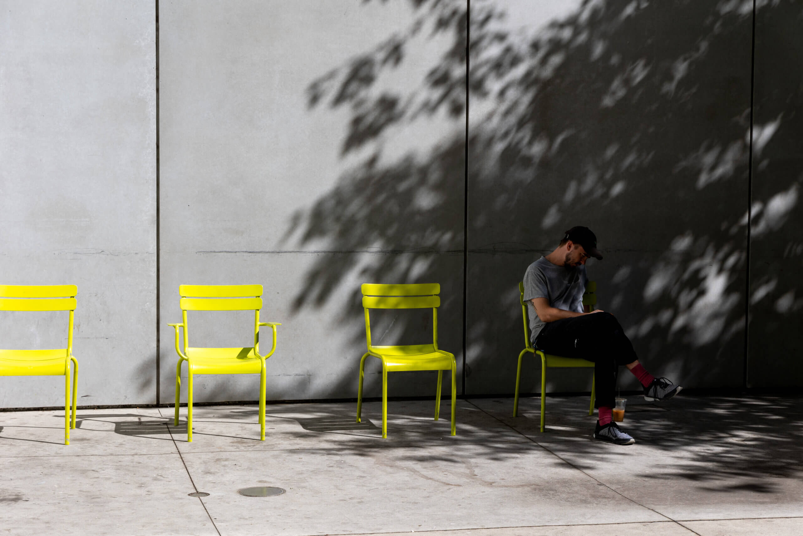 A photo of four fluorescent chairs facing a concrete wall in New York, with a man sitting on one chair, adding a touch of human presence to the minimalist urban scene