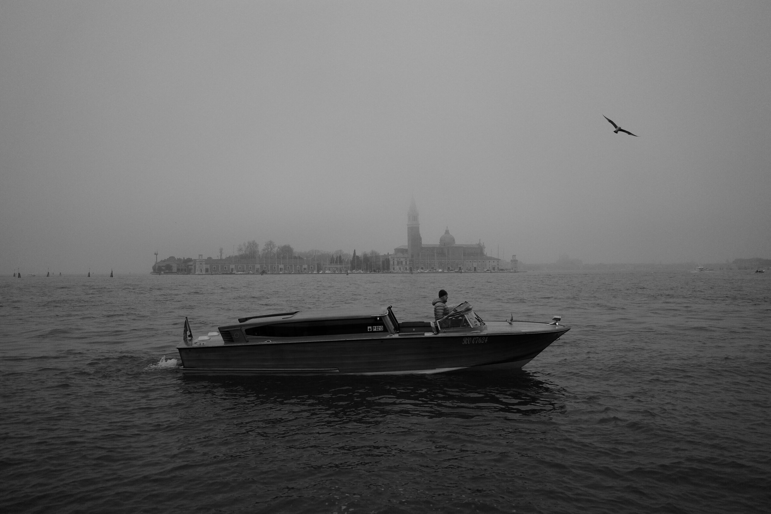 A stunning wooden boat gliding on the water in front of the San Giorgio Maggiore church in Venice, with a seagull flying above