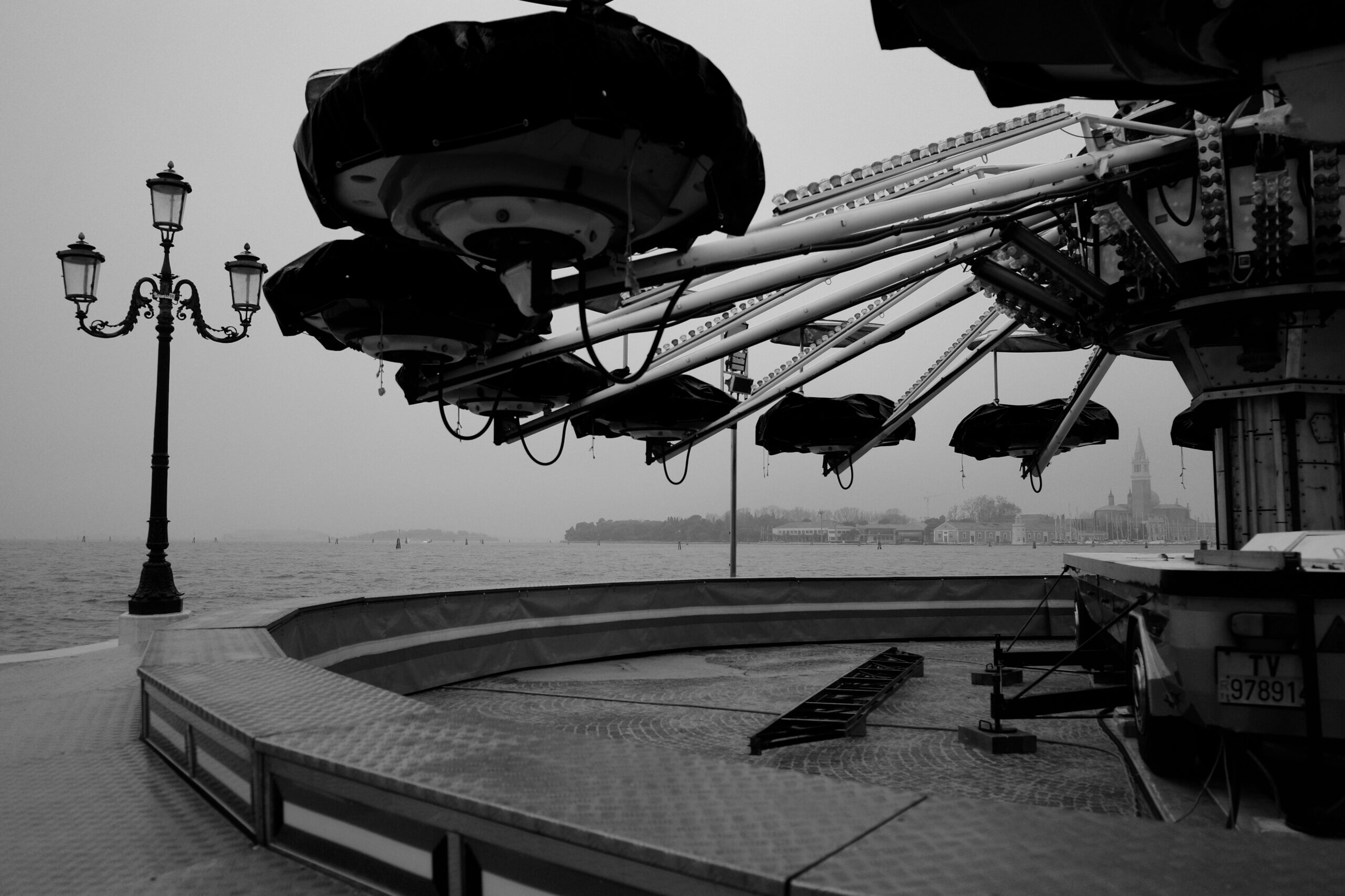 A black and white photo of a carousel in the foreground, with the San Giorgio Maggiore church in Venice enveloped in mist over the water in the background.