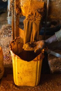 A photo of an Ethiopian artisan crafting chili powder, with bright orange powder emerging from a machine into their hand