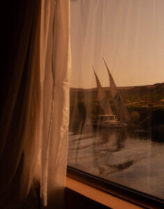 A traditional felucca sailing on the Nile River, seen through the window of a cruise ship.