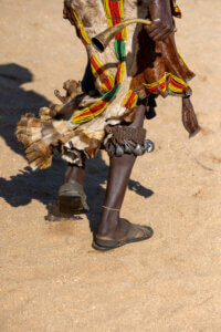 A photo of a Hamar woman’s legs adorned with animal skin and ornaments, dancing with a horn during the bull-jumping ceremony in Ethiopia to summon men for whipping
