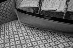 A photo of a model ship placed on a patterned sofa at the Annecy braderie, blending nautical artistry with vintage decor.