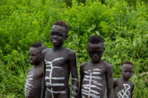 A photo of four young Mursi children in Ethiopia, adorned with white paint decorations, welcoming visitors to their village.