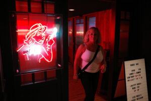A woman in the foreground at the Rodeo Bar in Dallas mirrors the pose of a red neon sign depicting a cowgirl