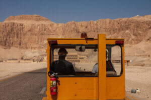 A mini train approaching the Temple of Hatshepsut in Luxor, Egypt, along the scenic road leading to the ancient site.