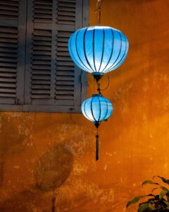 A blue traditional lantern in Hoi An, Vietnam, set against the warm ochre-colored wall, showcasing the town's iconic colors