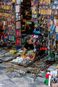 A silhouetted vendor sitting in front of a tool stall in Hanoi, Vietnam, surrounded by an array of diverse tools for sale