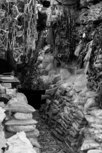A black-and-white photo of a woman stretching her legs over bags of hardware in her shop in Hanoi, Vietnam